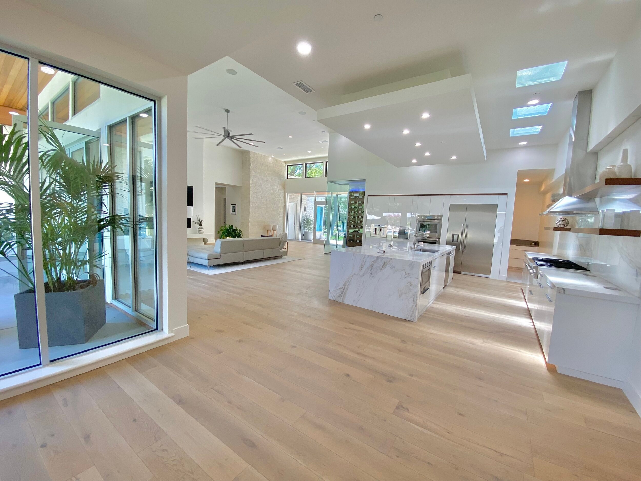 Open kitchen and living spaces with pale wood floors, high ceilings and broad sliding glass doors
