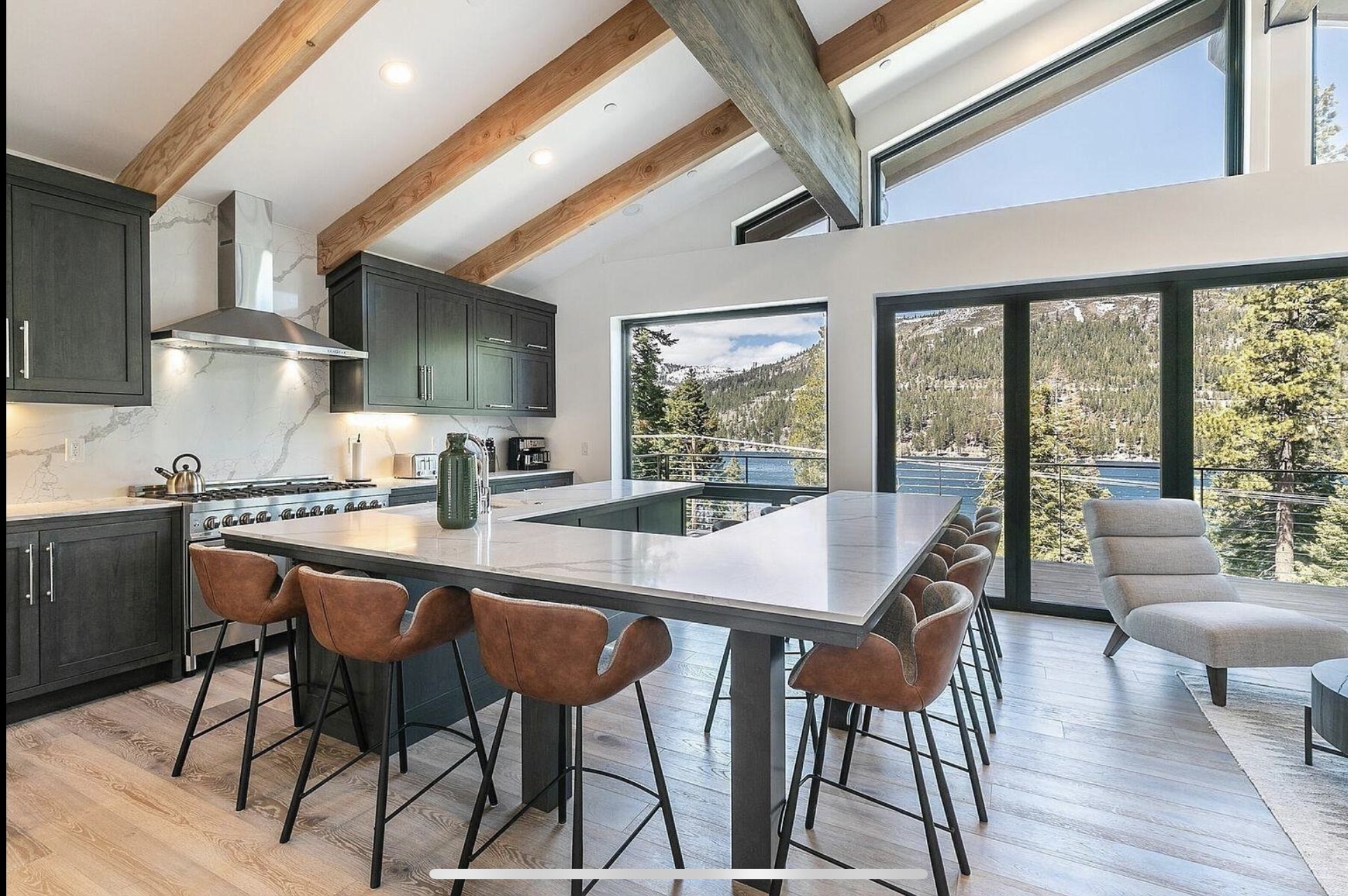 Kitchen with dark cabinetry, a pale stone island and leather counter stools